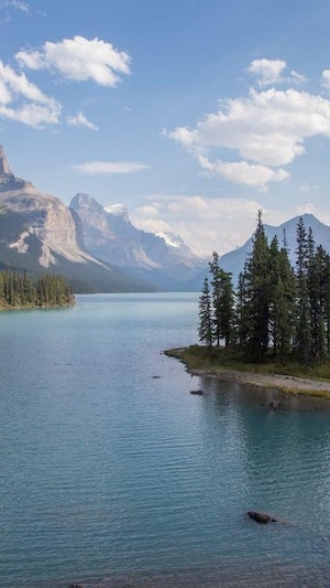 An island in the middle of a crystal-clear lake surrounded by coniferous forests and tall mountains.