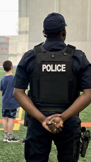 Un policier d'origine afro-descendante regarde des jeunes s'amuser.