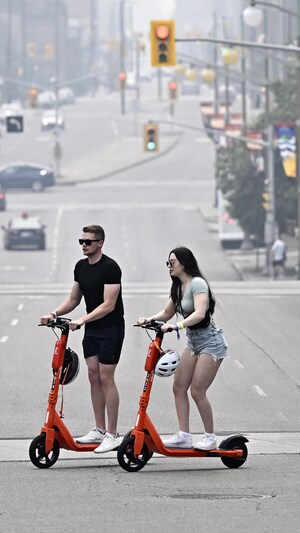 Un homme et une femme traversent une rue sur des trottinettes électriques.