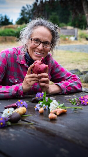 Fiona Hamersley assise à une table en bois avec des fleurs posée dessus, tenant entre ses mains une pomme de terre à la forme de cœur, à la ferme Metchosin, dans le sud de l'île de Vancouver, en août 2024.