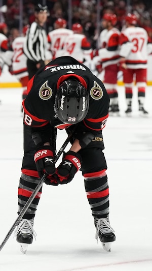 Un joueur de hockey a la mine basse devant ses adversaires qui célèbrent leur victoire.