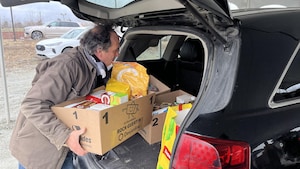 Un homme place un panier de provisions dans le coffre d'une voiture.