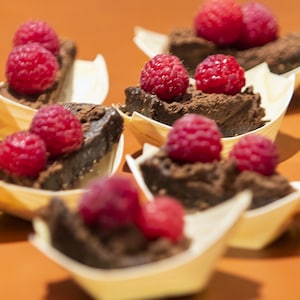 Des brownies véganes, décorés de framboises et servis dans de petites barquettes de carton.