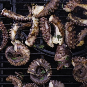 Des morceaux de pieuvre cuisent sur une grille de barbecue.