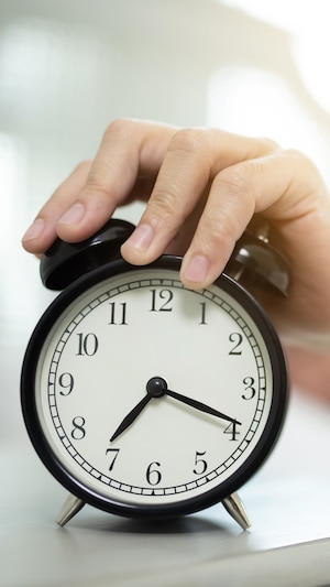 Plan rapproché la main d'une personne posée sur un réveille-matin, au sortir du lit. 