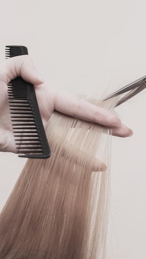 Une coupe de cheveux réalisée avec un peigne dans une main, un ciseau dans l'autre