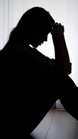 Une femme est accroupie dans le noir dans une chambre et se tient la tête dans les mains. 