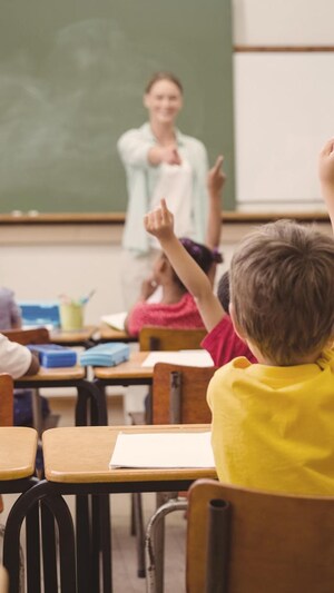 Élèves en classe qui lèvent la main avec professeur derrière.