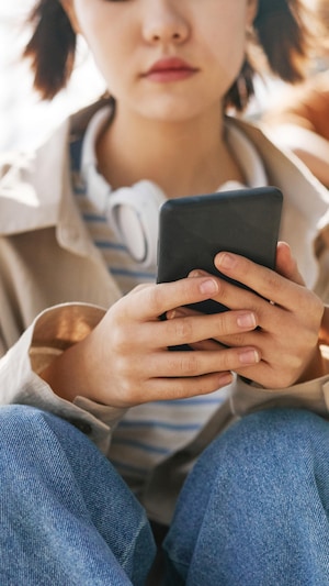 Une adolescente regarde son téléphone cellulaire pendant d'un groupe de jeunes, assis derrière elle, semble se moquer.
