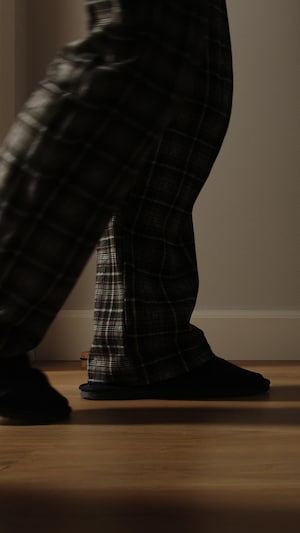 Vue des jambes d'un homme en pyjama déambulant dans un couloir sombre.