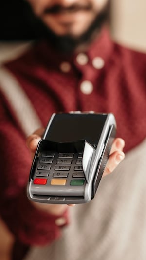Un homme vêtu d'un tablier tend un terminal de paiement. 