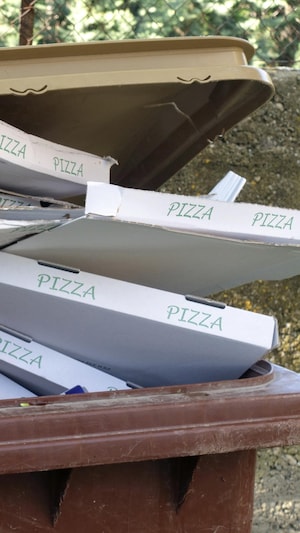 Plusieurs boîtes de pizza dans une grande poubelle.