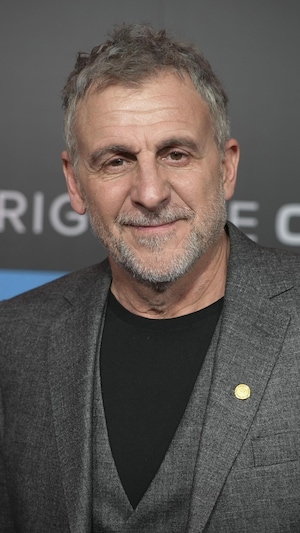 Patrick Huard, souriant, qui pose devant une affiche de la série « Bon Cop, Bad Cop ».