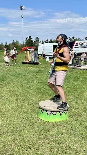Un musicien en costume d'abeille joue de la guitare sur une estrade verte au milieu d'un parc.