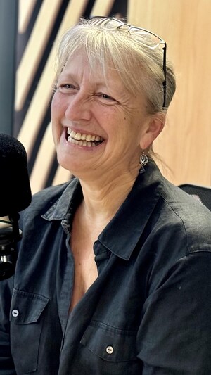 Une femme souriante devant un micro dans un studio de radio.