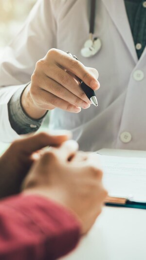 Les bras d'un médecin et de sa patiente discutant, assis à un bureau.