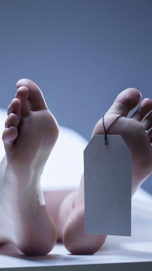 Photo des pieds d'une personne allongée sur une table recouverte d'un drap, avec une étiquette au pied.