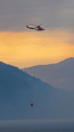 Un hélicoptère vole au-dessus d'une vaste étendue d'eau, dans un ciel orange de fumée. 