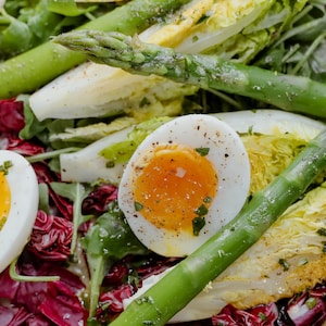 Une salade repas avec des œufs, des asperges et un mélange de laitues.