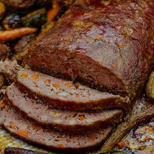 Un pain de viande cuit sur une plaque, entouré de légumes rôtis.