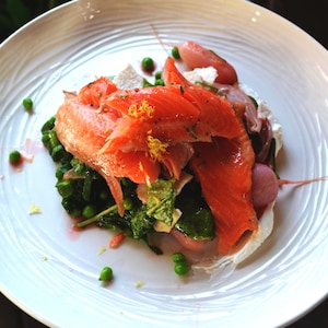 Truite fumée à chaud et salade de radis, de petits pois et d’oignons nouveaux dans une assiette blanche.