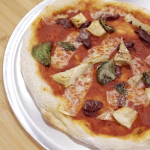 Une grande pizza tomates, olives, artichauts et fromage présentée sur une plaque à pizza.