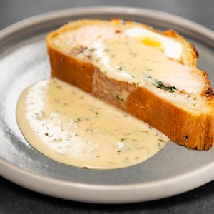 Un koulibiac servi dans une assiette ronde, (feuilleté de saumon) nappé d'une sauce au vin blanc aromatisée aux fines herbes.