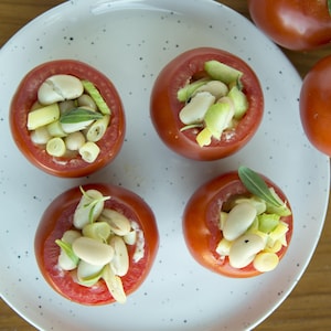 Une assiette avec 4 tomates farcies et des tomates sur vigne à côté.