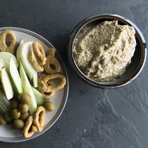 Un bol de trempette est accompagné de crudités, d'olives et de pains bâtons.