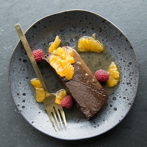Le dessert, dans une assiette, est garni de framboises et de clémentines.