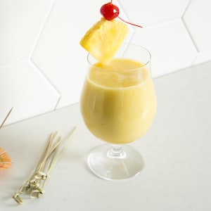 Le verre de pina colada est garni d'un morceau d'ananas et d'une cerise.