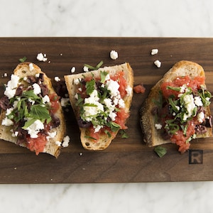 Trois morceaux de pain garnis de salade de tomates sont sur une planche de bois.