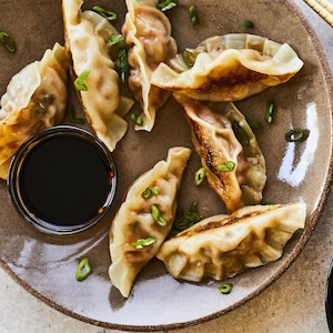 Une demi-douzaine de dumplings sont dans une grande assiette à côté d'un petit bol de sauce.