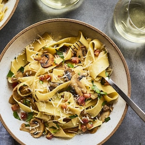 Un plat de pappardelles aux champignons et à la pancetta sur la table.