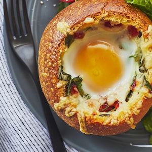 Œufs dans un bol de pain est accompagné d'une salada dans une assiette.