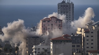 Au loin, la mer Méditérranée. En premier plan, des bâtiments desquels s'échappe de la fumée après une attaque aérienne.