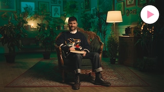 Arnaud Granata est assis dans un fauteuil sur un tapis dans une pièce entourée de plantes et de tableaux botaniques.