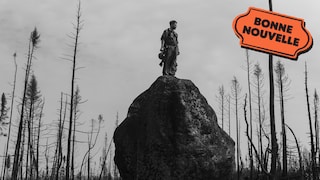 Une photo en noir et blanc d'un pompier debout sur un rocher qui fixe une forêt ravagée par le feu. 