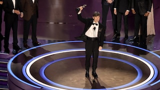 L'homme lève une statuette dans les airs sur scène devant d'autres acteurs.