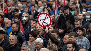 Un homme dans une foule tient une pancarte avec le visage de Vladimir Poutine barré en rouge.