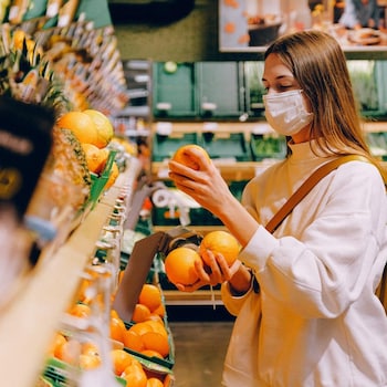Une jeune femme masquée choisit des oranges au marché.