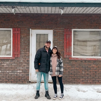 Le couple est dehors, l'hiver, devant une maison de brique et sourit pour la photo. 