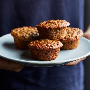 Une personne tient une assiette ronde contenant cinq muffins. 