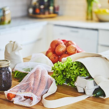 Des sacs écologiques contenant des aliments sont déposés sur un comptoir de bois.