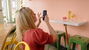 Une femme qui prend trois cocktails colorés en photo avec son téléphone.