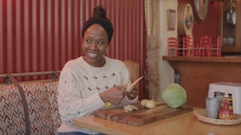 Une personne est assise à une table d'un restaurant et tranche des légumes. 