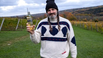 Un homme devant un vignoble tenant une bouteille de vin.