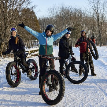 Geneviève O'Gleman accompagnée de plusieurs personnes pratiquant le vélo à pneus surdimensionnés (fatbike en anglais) en hiver.