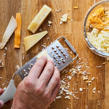 Une personne râpe plusieurs petits bouts de fromages à pâte ferme pour faire un mélange de fromages maison.