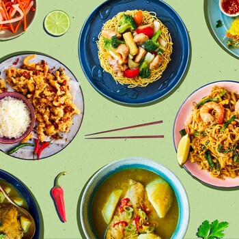Plusieurs plats asiatiques dans des assiettes avec des baguettes, de la lime, des piments rouges et de la coriandre.